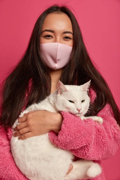girl in pink wearing mask holding a white cat