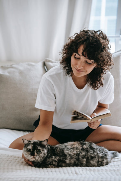 Girl with a book happy touching cat at home