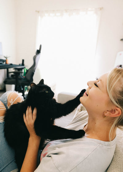 Girl smiling while playing with a black cat at home 