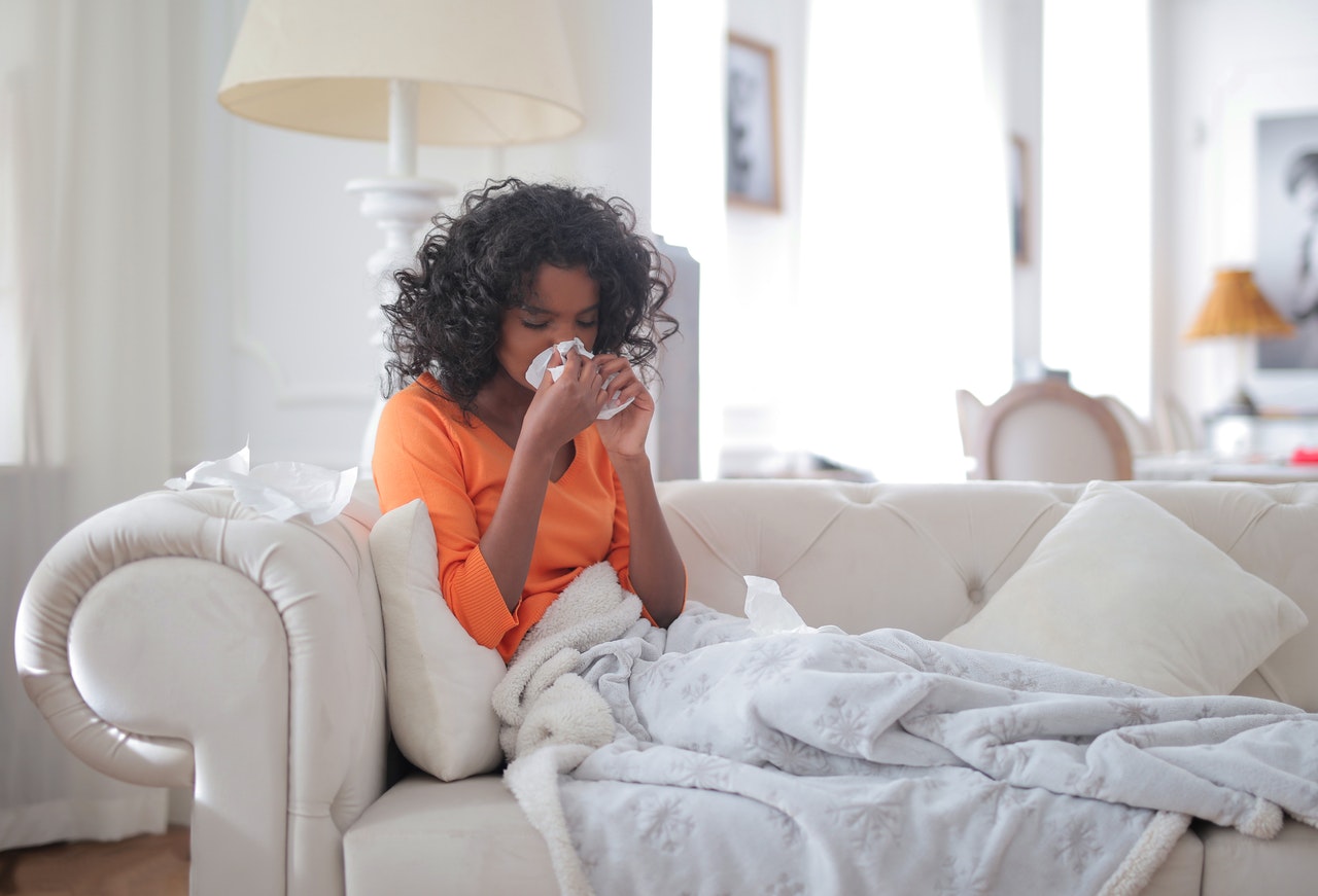 Girl in orange shirt sneezing at home with cat dander 